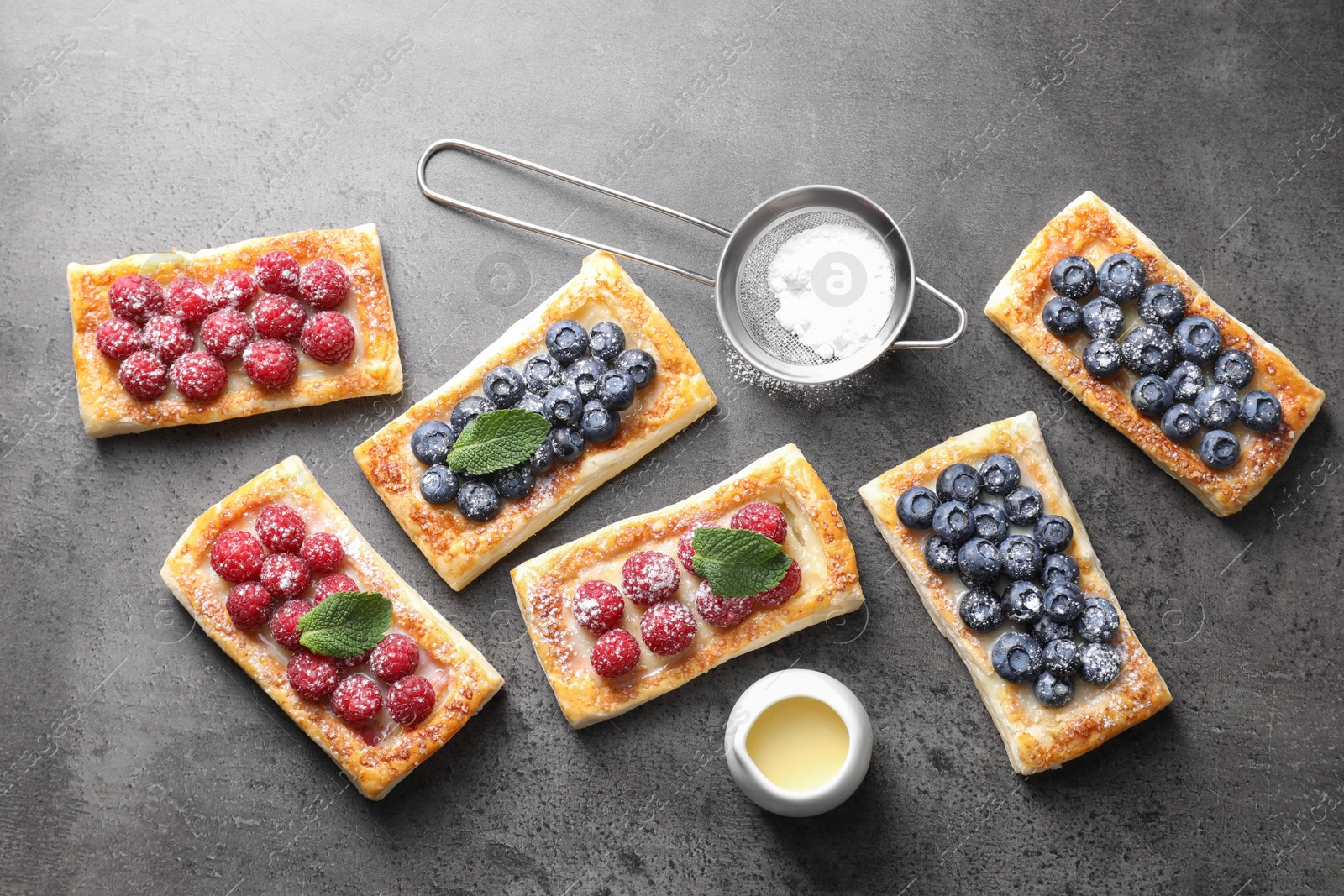 Photo of Tasty puff pastries with berries and powdered sugar on grey table, flat lay