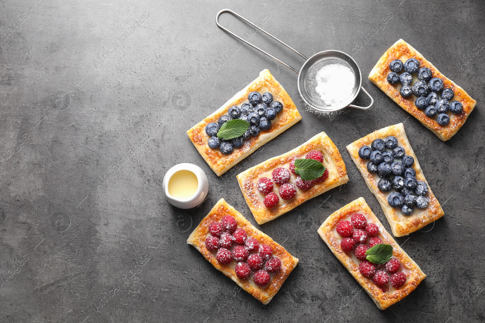 Photo of Tasty puff pastries with berries and powdered sugar on grey table, flat lay. Space for text