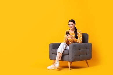 Photo of Smiling woman with smartphone sitting on armchair against yellow background. Space for text