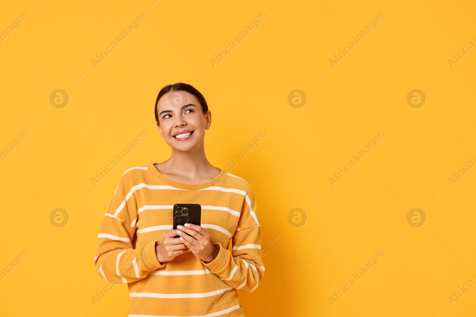 Photo of Smiling woman with smartphone on yellow background. Space for text