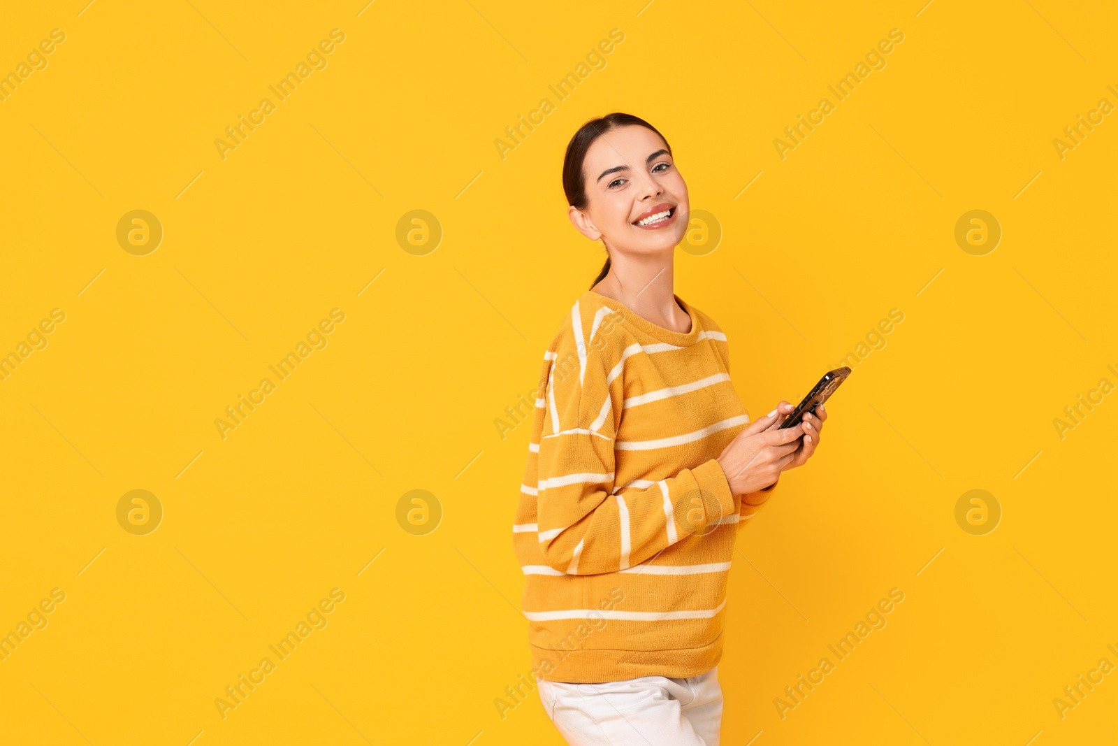 Photo of Smiling woman with smartphone on yellow background. Space for text