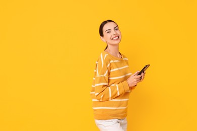 Photo of Smiling woman with smartphone on yellow background. Space for text