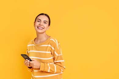 Photo of Smiling woman with smartphone on yellow background. Space for text