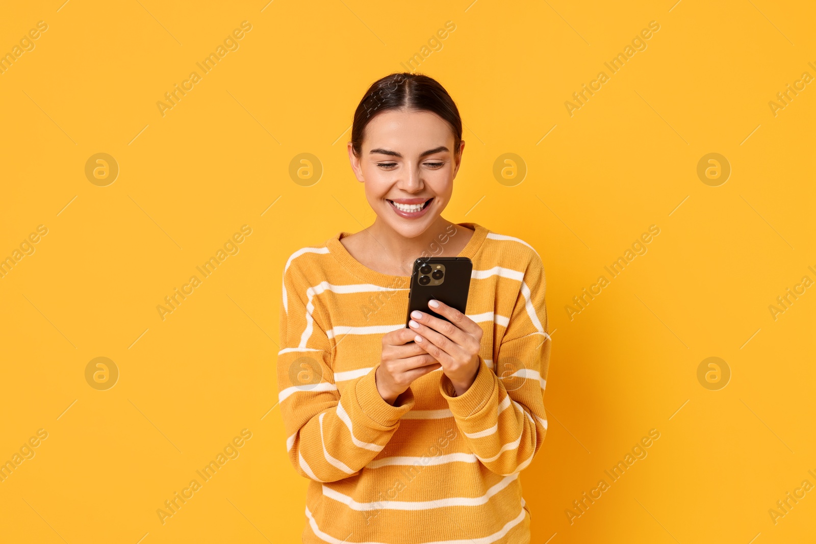 Photo of Smiling woman with smartphone on yellow background