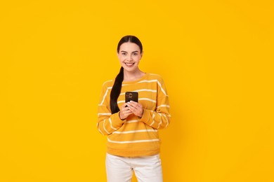 Photo of Smiling woman with smartphone on yellow background