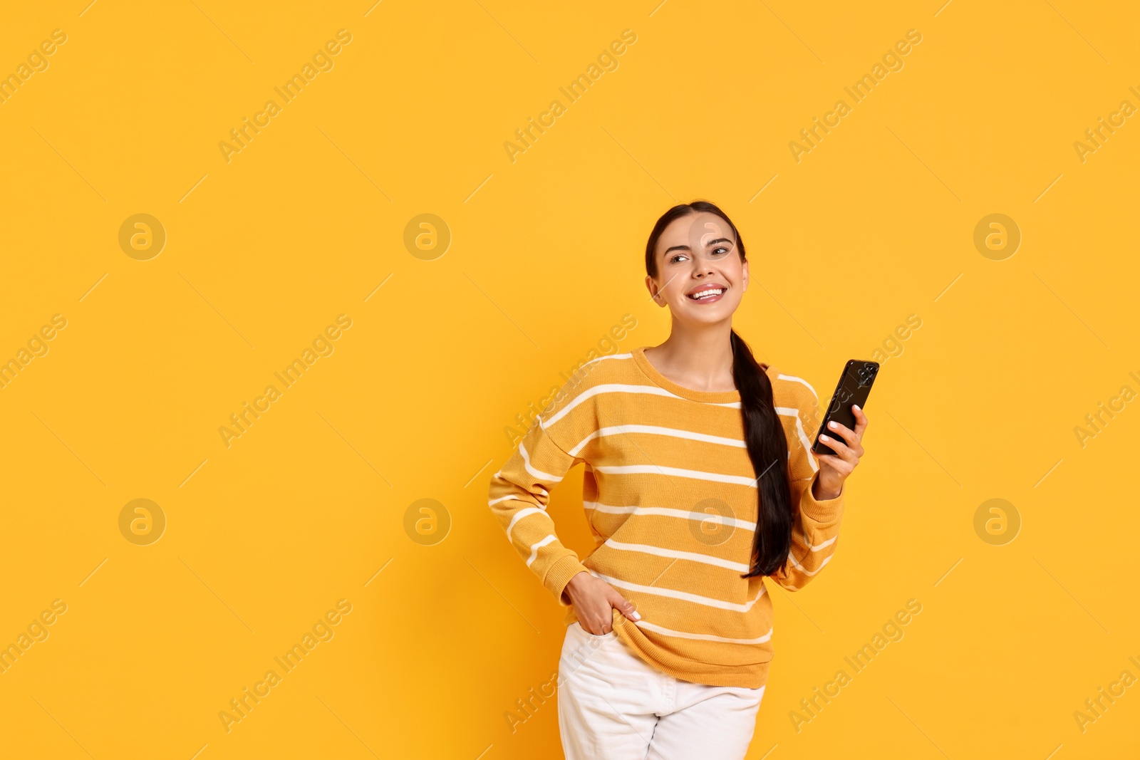 Photo of Smiling woman with smartphone on yellow background. Space for text