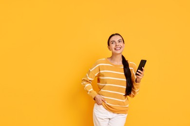 Smiling woman with smartphone on yellow background. Space for text