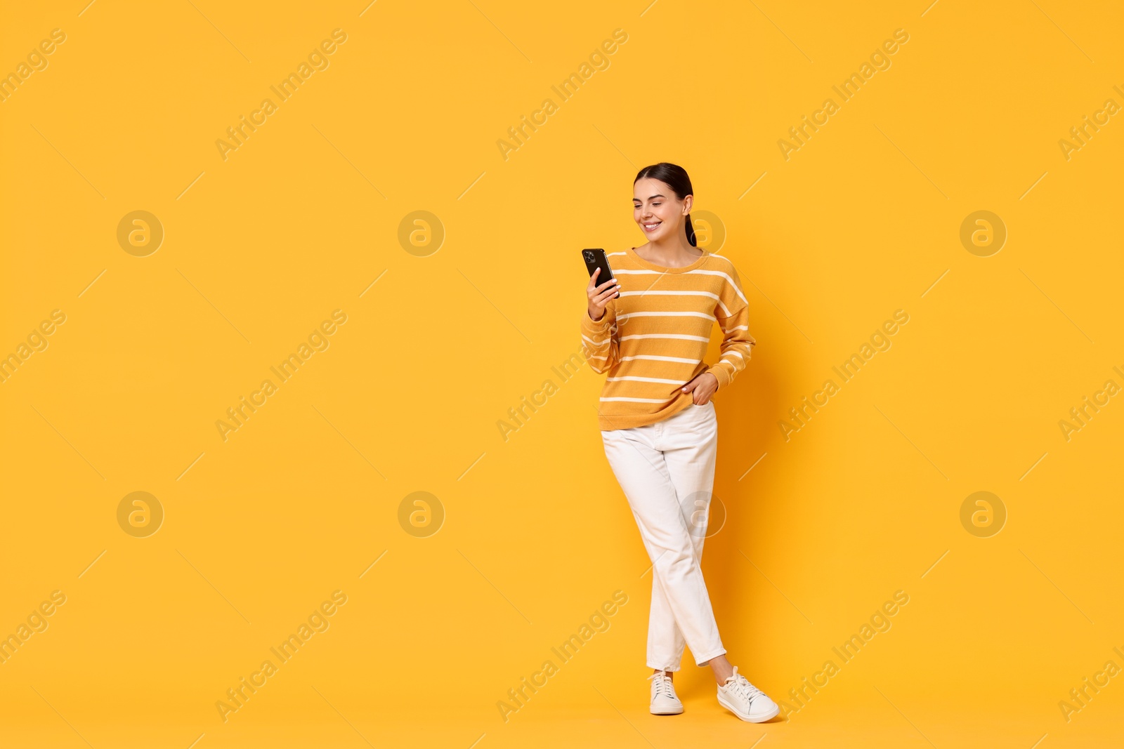 Photo of Smiling woman with smartphone on yellow background. Space for text