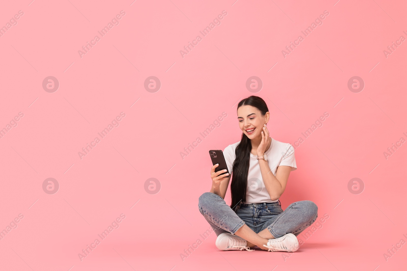 Photo of Smiling woman with smartphone on pink background. Space for text