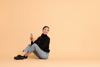 Photo of Smiling woman with smartphone on beige background. Space for text