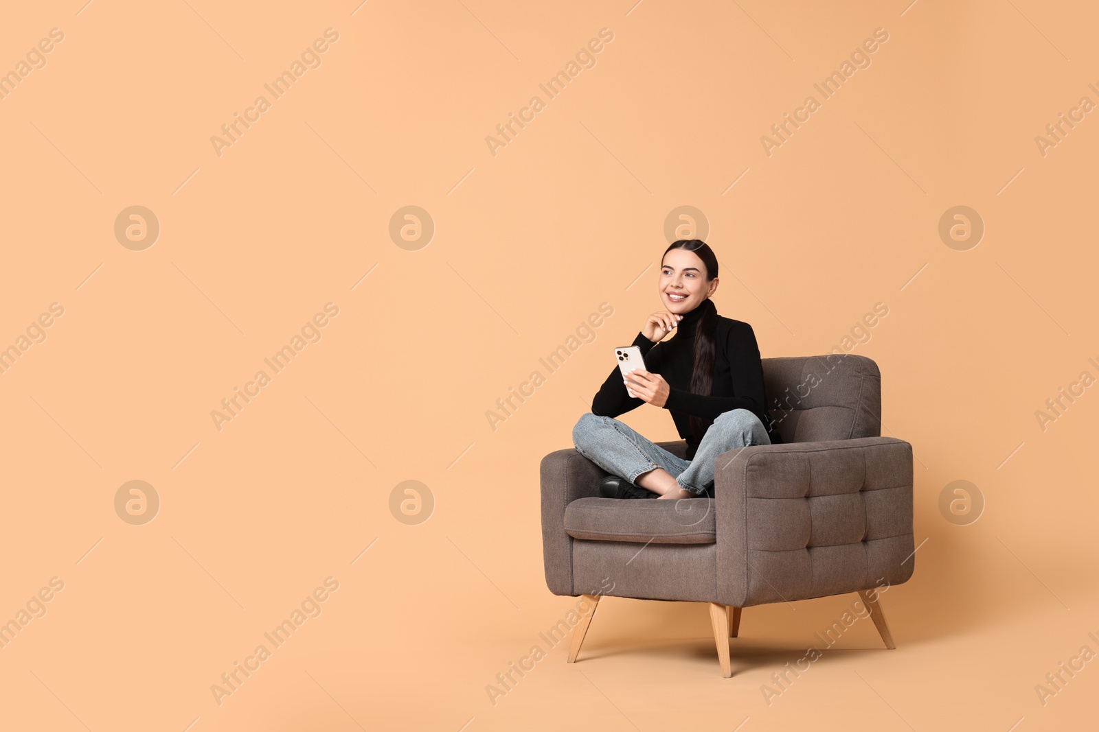 Photo of Smiling woman with smartphone sitting on armchair against beige background. Space for text