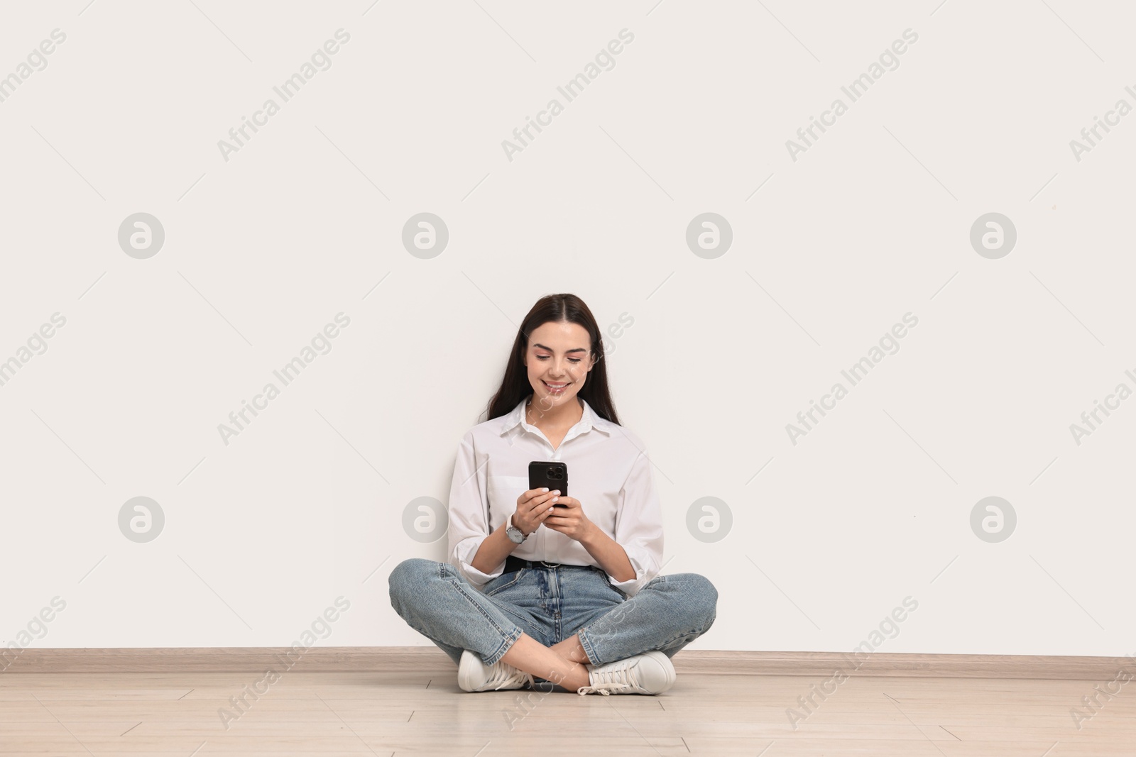 Photo of Smiling woman with smartphone on floor against white background