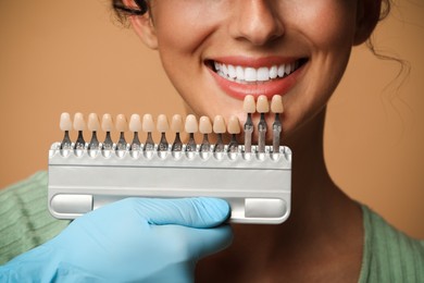 Photo of Doctor checking young woman's teeth color on beige background, closeup. Dental veneers