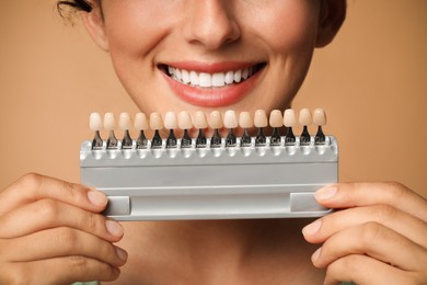 Photo of Smiling woman with teeth color samples on beige background, closeup. Dental veneers