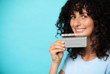 Happy young woman with teeth color samples on light blue background, space for text. Dental veneers