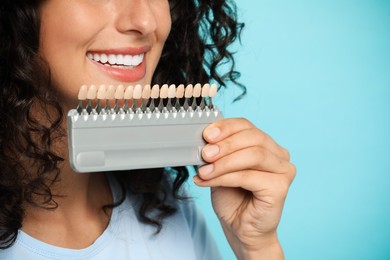 Smiling woman with teeth color samples on light blue background, closeup. Dental veneers