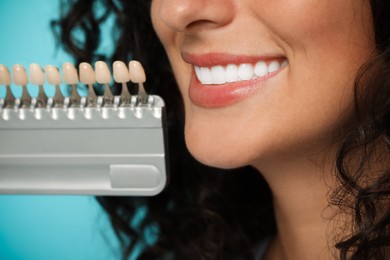 Smiling woman with teeth color samples on light blue background, closeup. Dental veneers