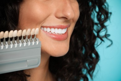 Smiling woman with teeth color samples on light blue background, closeup. Dental veneers