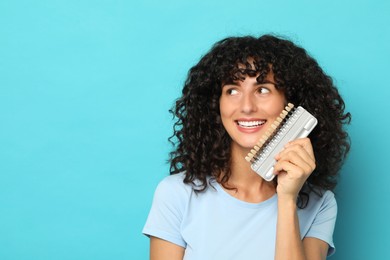 Happy young woman with teeth color samples on light blue background, space for text. Dental veneers