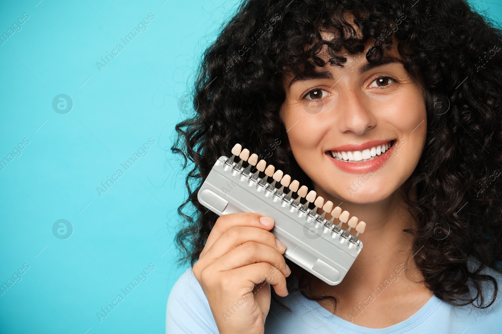 Photo of Happy young woman with teeth color samples on light blue background, space for text. Dental veneers