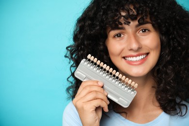 Photo of Happy young woman with teeth color samples on light blue background, space for text. Dental veneers