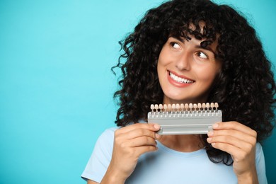 Happy young woman with teeth color samples on light blue background, space for text. Dental veneers