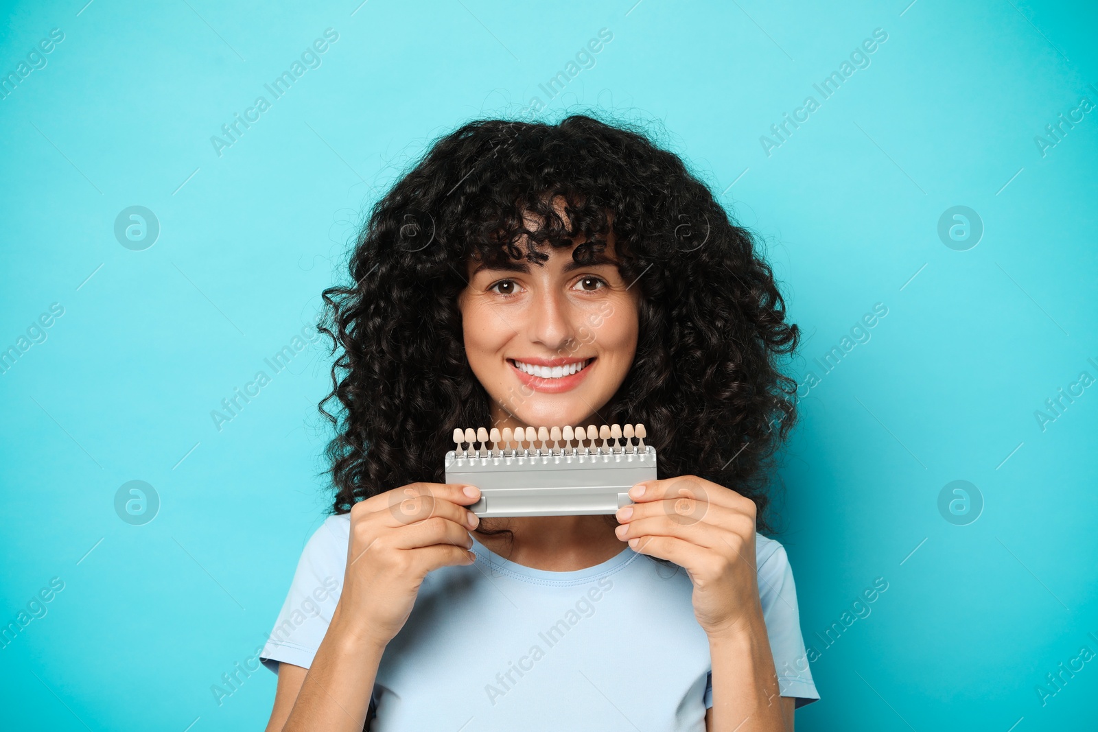 Photo of Happy young woman with teeth color samples on light blue background. Dental veneers