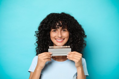 Photo of Happy young woman with teeth color samples on light blue background. Dental veneers