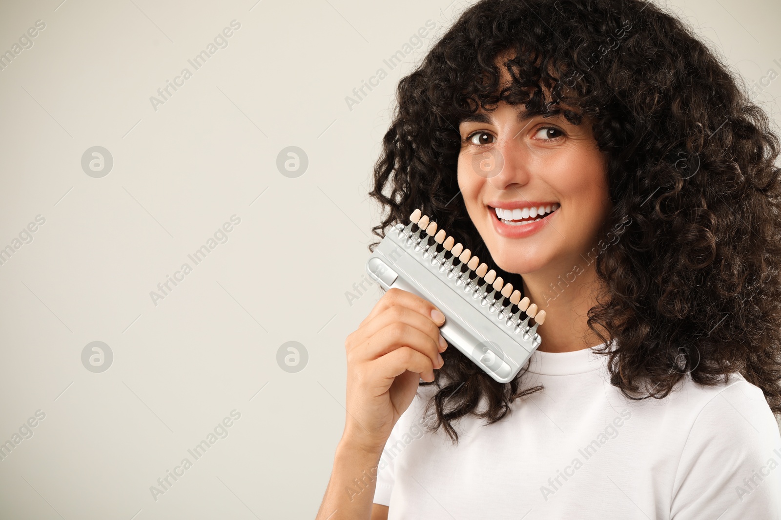 Photo of Happy young woman with teeth color samples on light grey background, space for text. Dental veneers