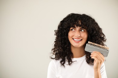 Happy young woman with teeth color samples on light grey background, space for text. Dental veneers