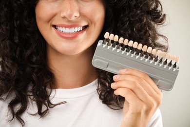 Photo of Smiling woman with teeth color samples on light grey background, closeup. Dental veneers