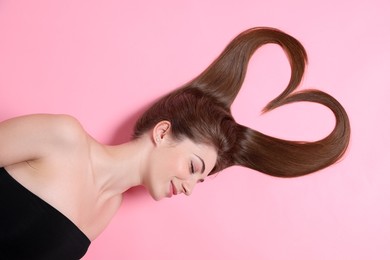 Beautiful young woman with hair in shape of heart on pink background