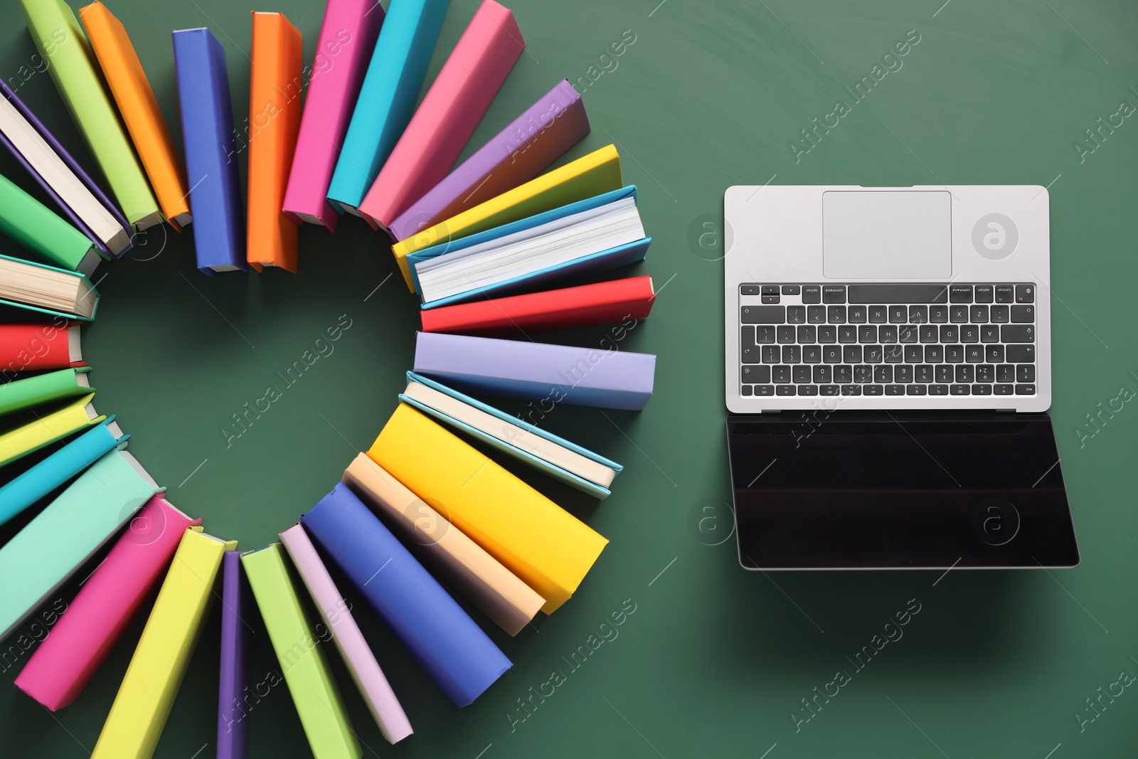 Photo of Heart made of many colorful books and laptop on green background, flat lay