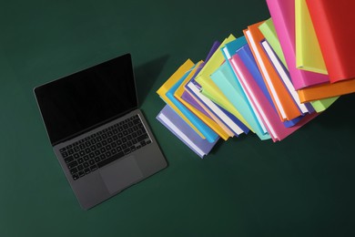 Stack of many colorful books and laptop on green background, above view