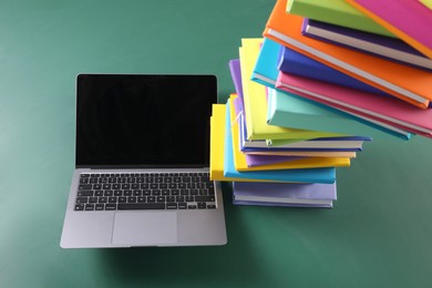 Photo of Stack of many colorful books and laptop on green background, above view