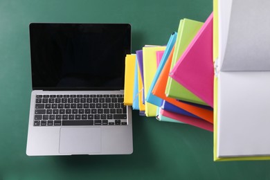 Stack of many colorful books and laptop on green background, above view