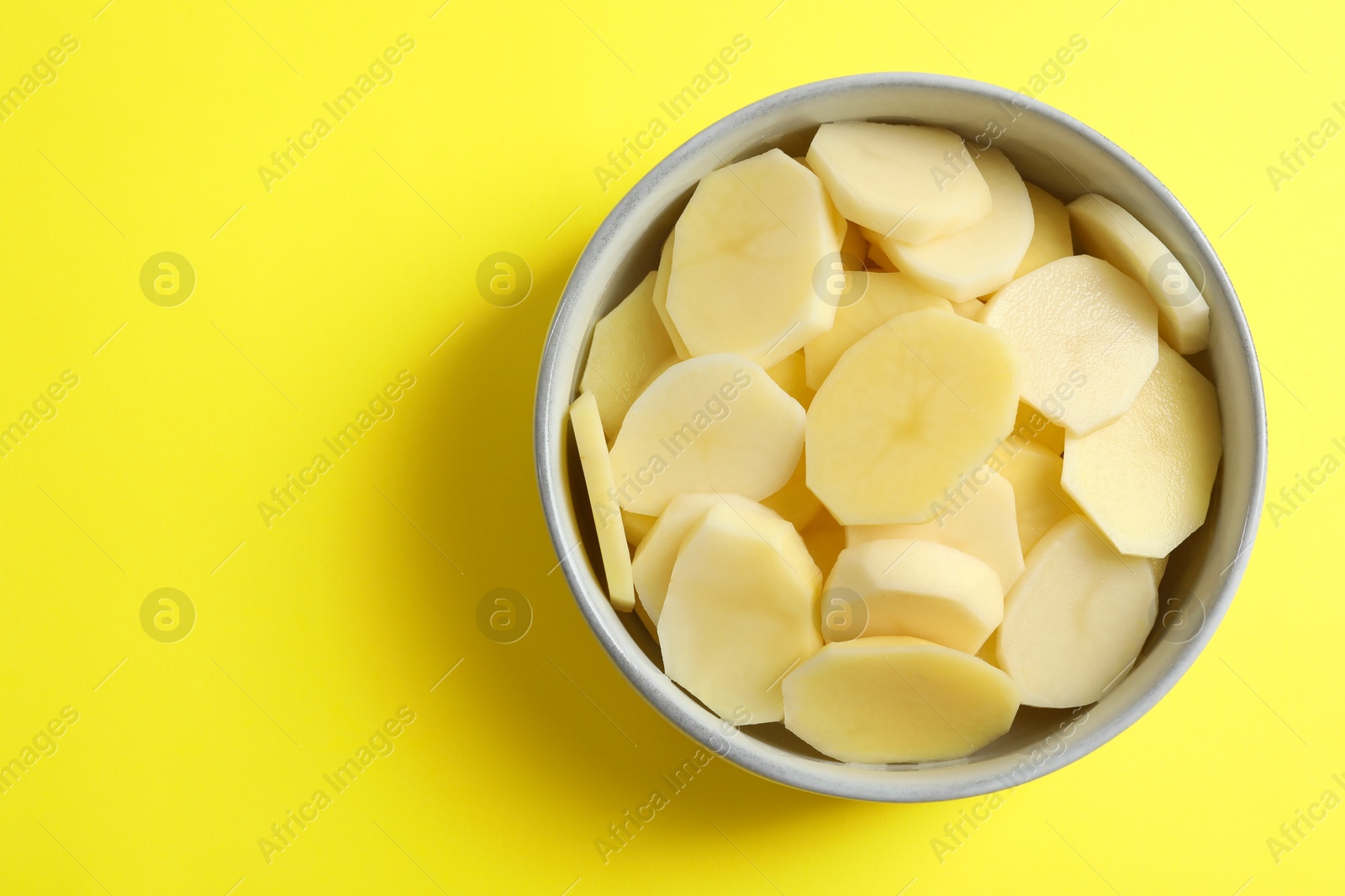 Photo of Cut fresh raw potatoes in bowl on yellow background, top view. Space for text