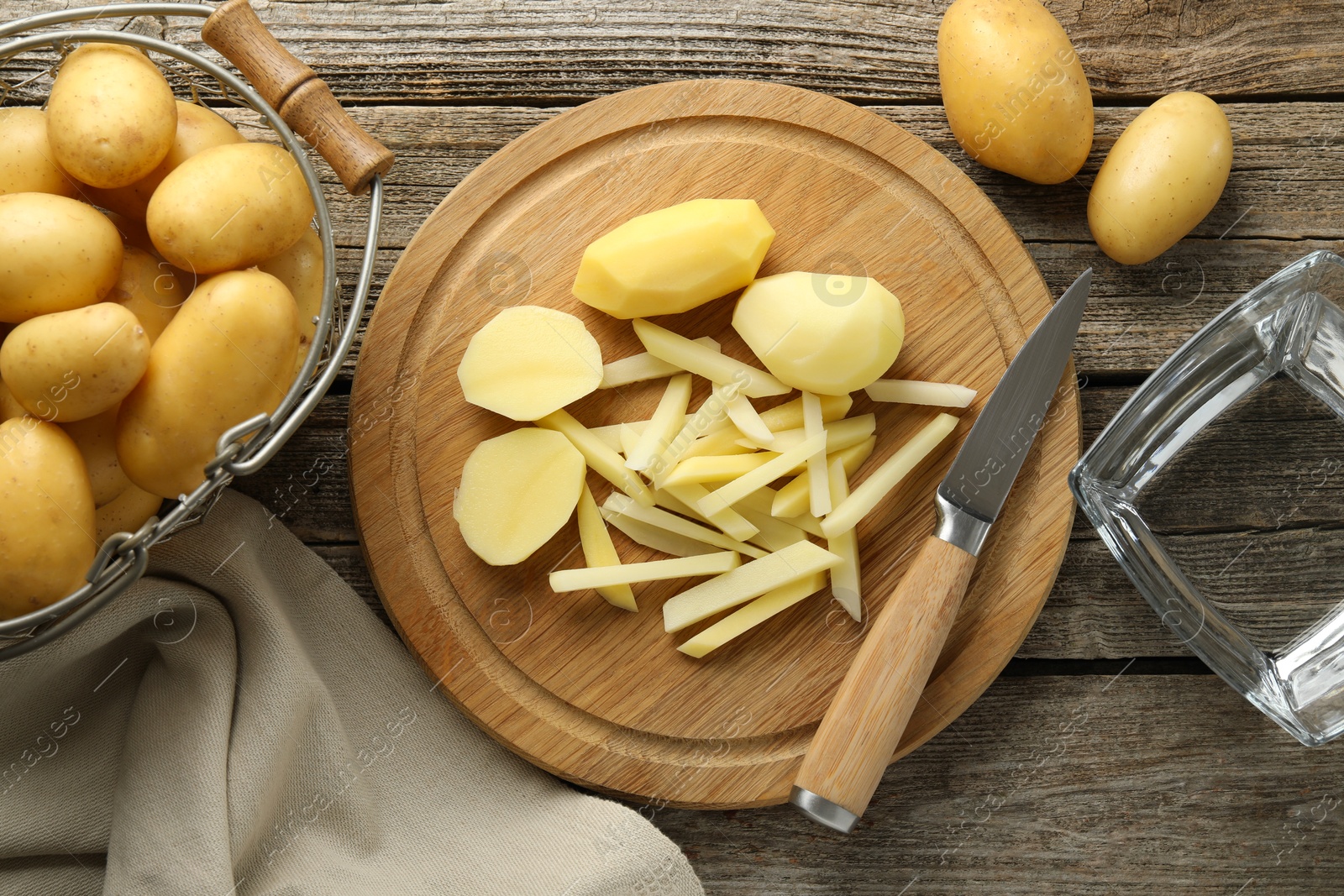 Photo of Whole and cut fresh raw potatoes near knife on wooden table, top view