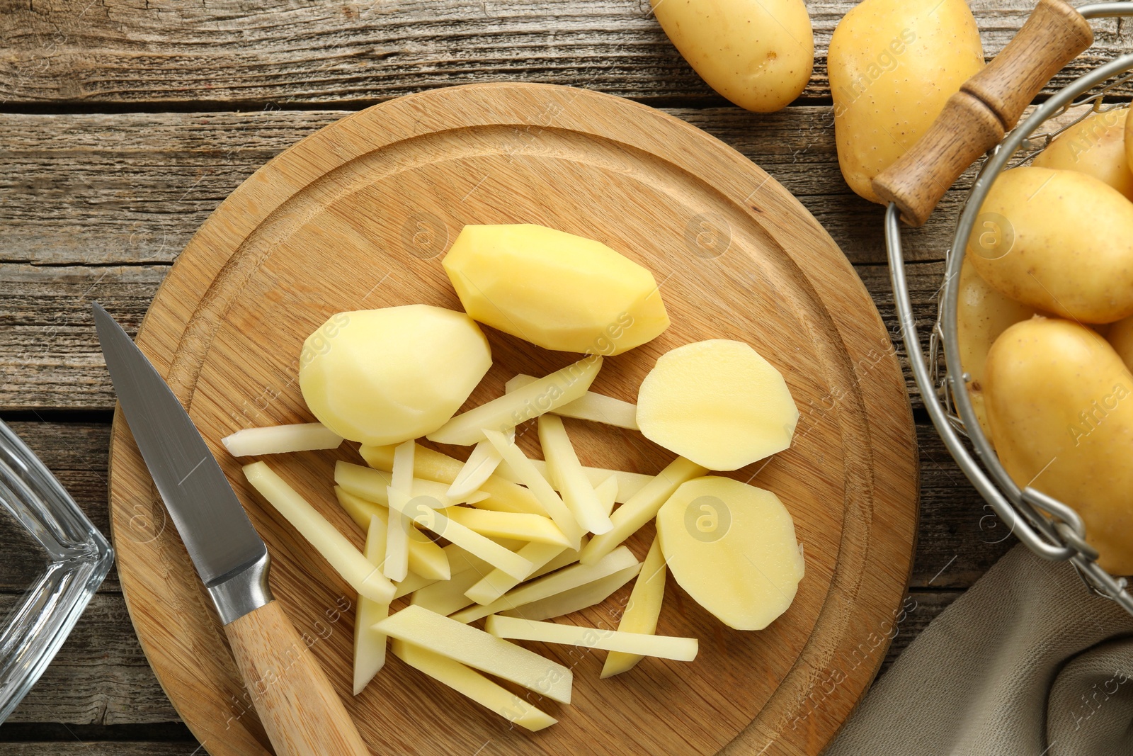 Photo of Whole and cut fresh raw potatoes near knife on wooden table, top view