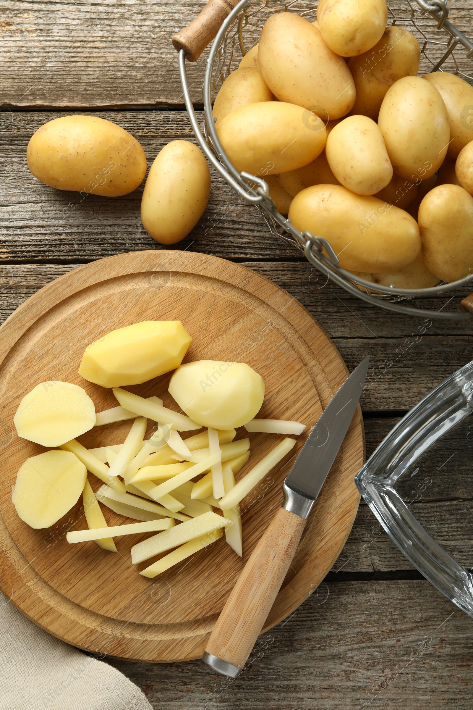 Photo of Whole and cut fresh raw potatoes near knife on wooden table, top view