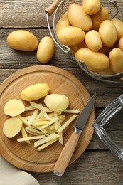 Whole and cut fresh raw potatoes near knife on wooden table, top view