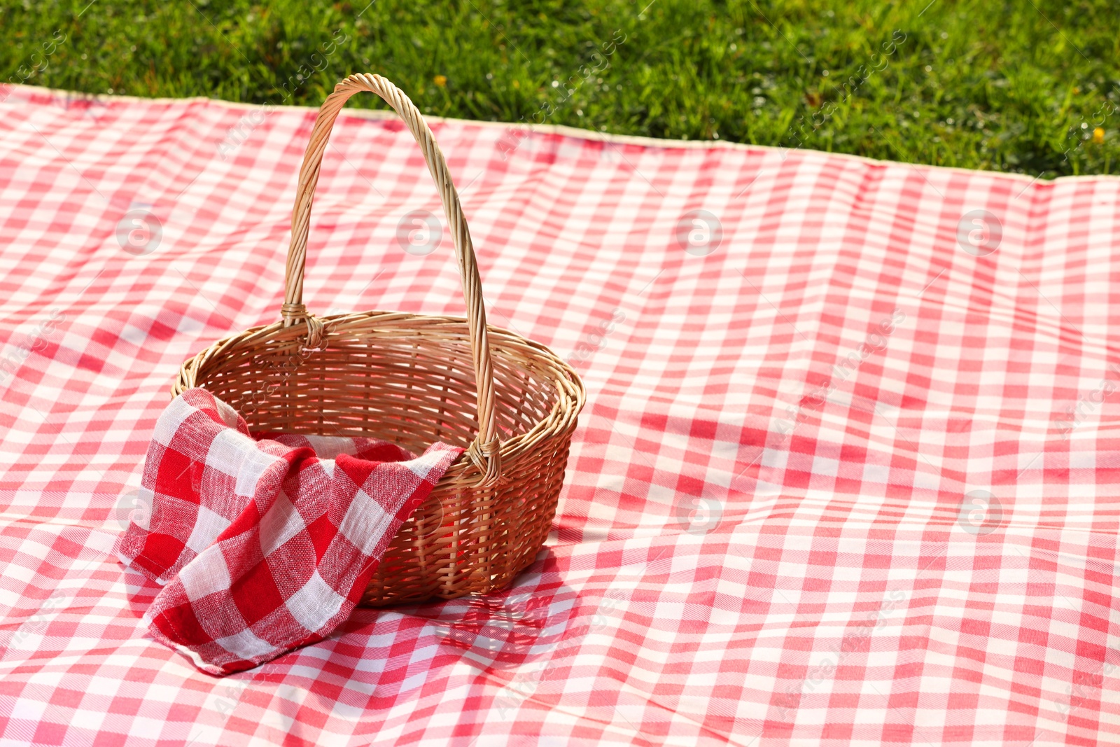 Photo of One picnic wicker basket with checkered napkin and blanket on green grass. Space for text