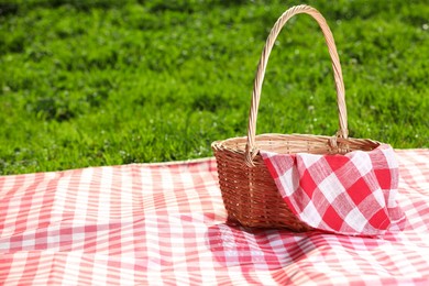 Photo of One picnic wicker basket with checkered napkin and blanket on green grass. Space for text