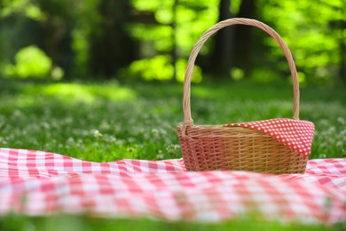 Photo of One picnic wicker basket with checkered napkin and blanket on green grass. Space for text