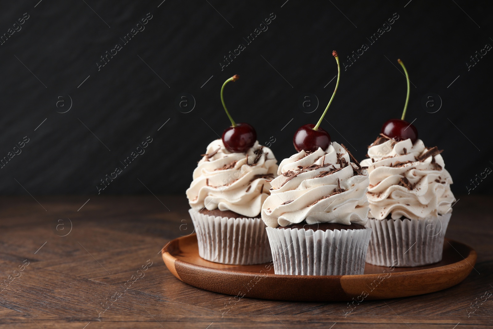 Photo of Delicious cupcakes with cream and cherries on wooden table, space for text