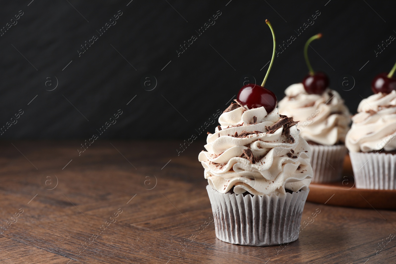 Photo of Delicious cupcakes with cream and cherries on wooden table. Space for text