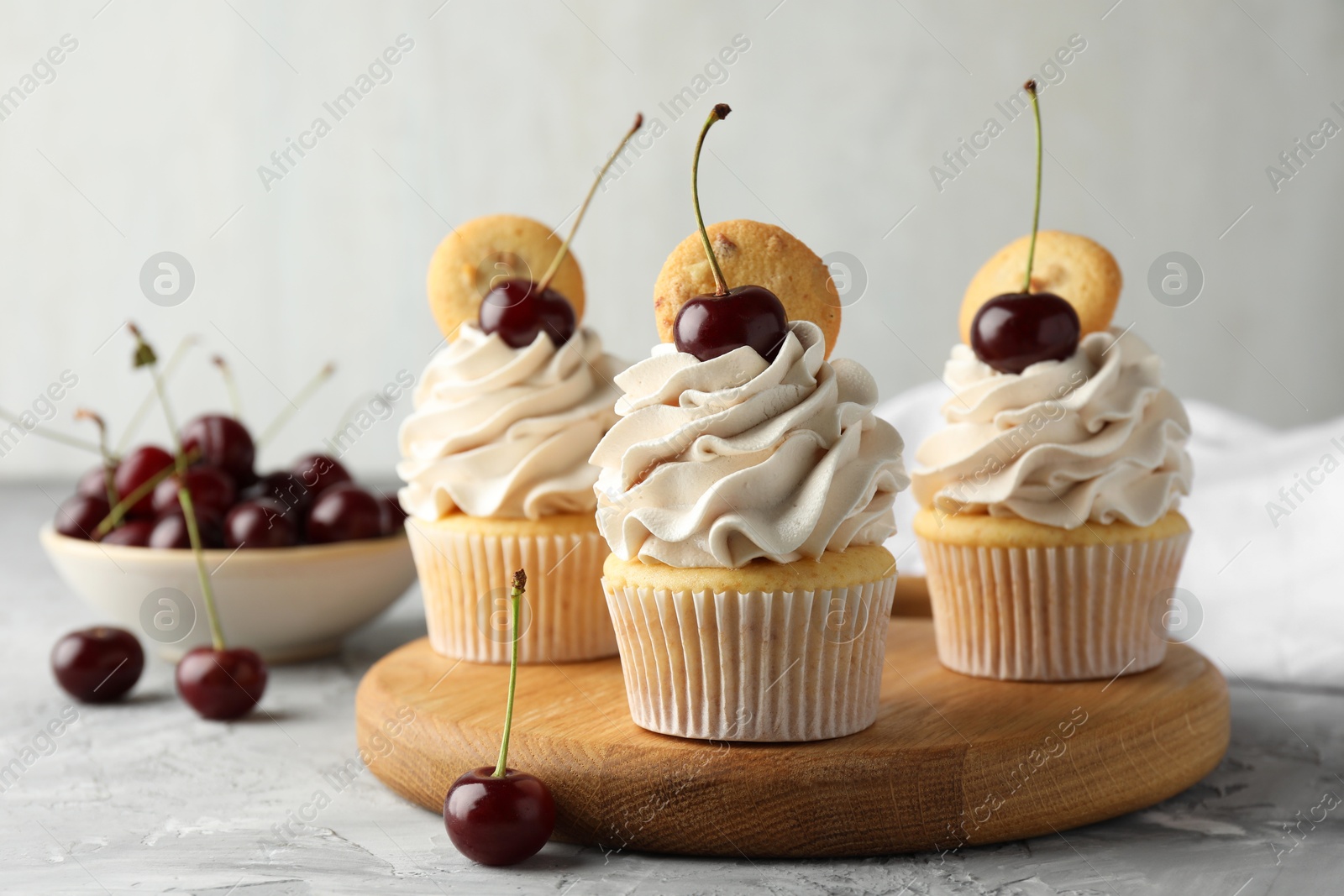 Photo of Delicious cupcakes with cherries and cookies on grey textured table, closeup