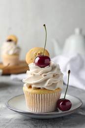 Photo of Delicious cupcake with cherries and cookie on grey textured table, closeup