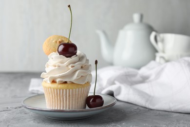 Photo of Delicious cupcake with cherries and cookie on grey textured table, closeup. Space for text