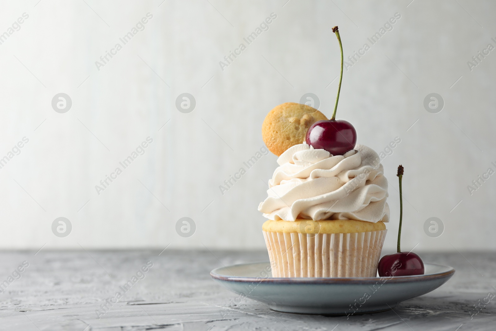 Photo of Delicious cupcake with cherries and cookie on grey textured table, closeup. Space for text